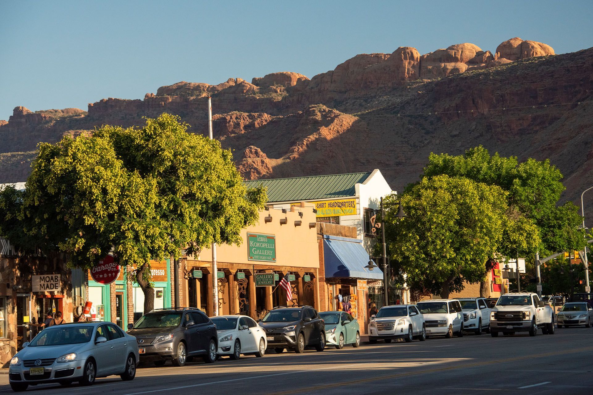 Street view with cars parked along the side, buildings, and mountains in the background.