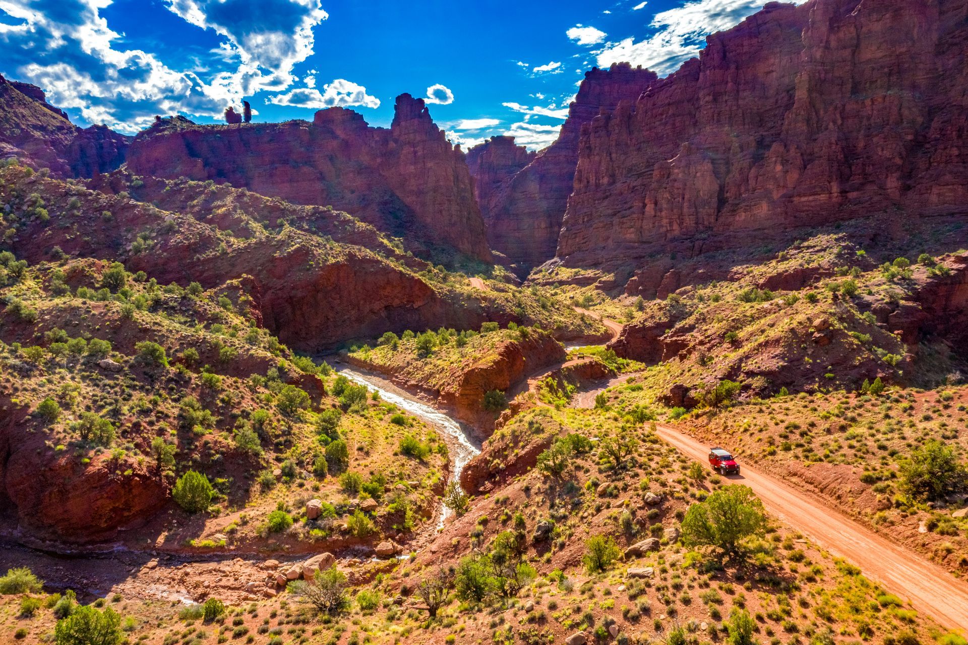 Red rock canyon with a winding dirt road and a small red car.