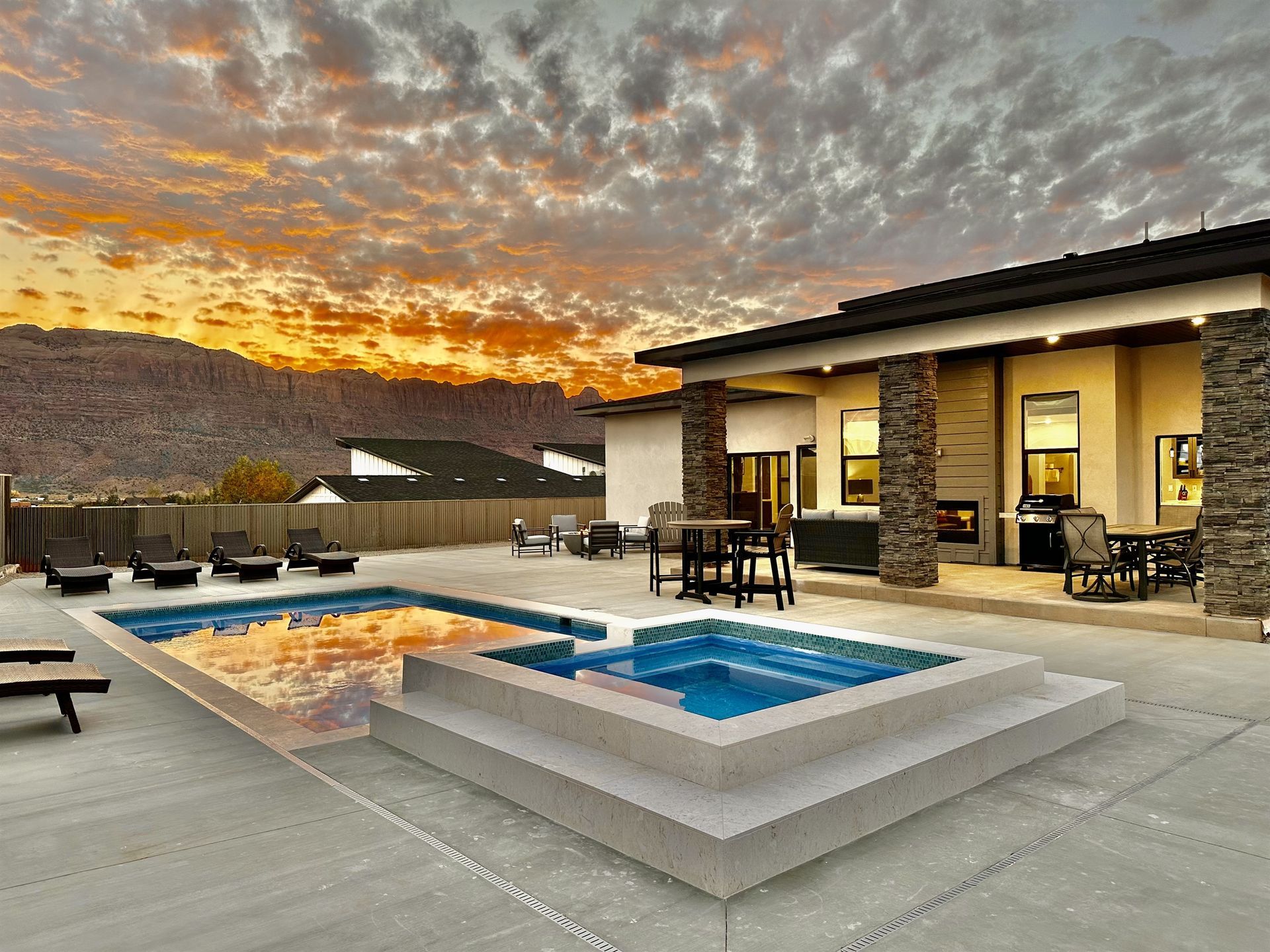 Backyard with a pool and spa at sunset. Modern home with patio furniture and mountain backdrop.