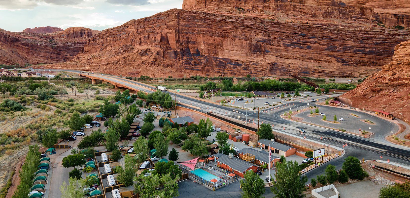 Aerial view of a campground with a road and bridge in front of a large red rock formation.