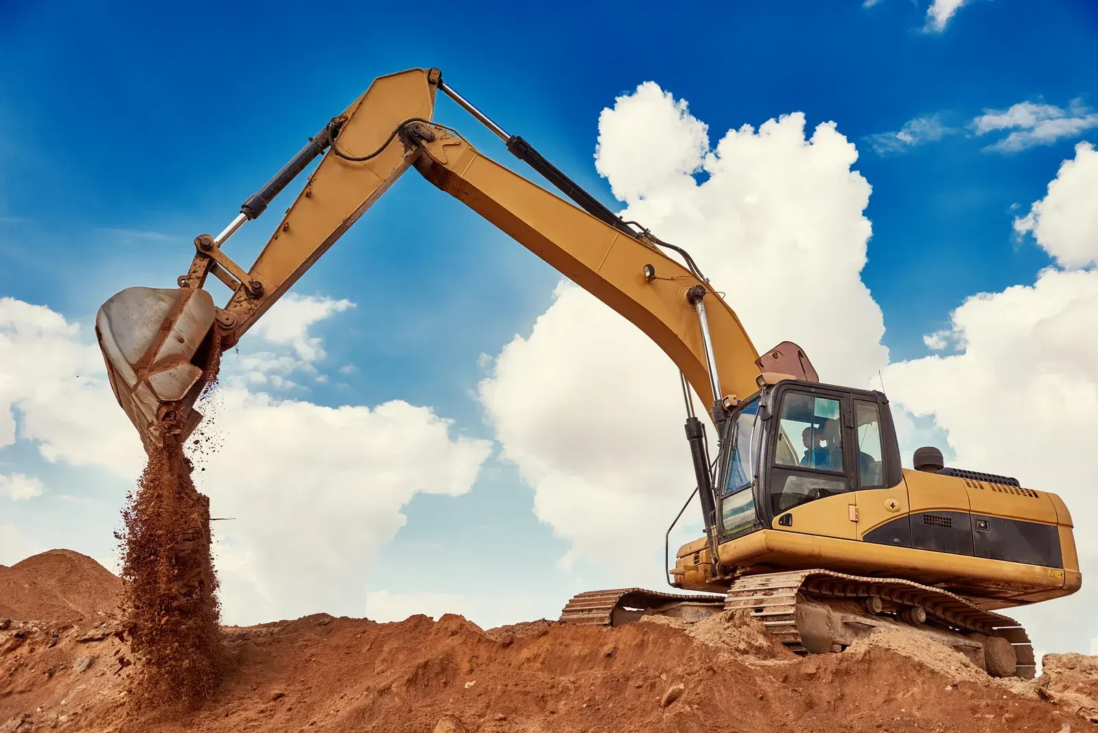 Yellow excavator digging dirt at a construction site under a blue sky