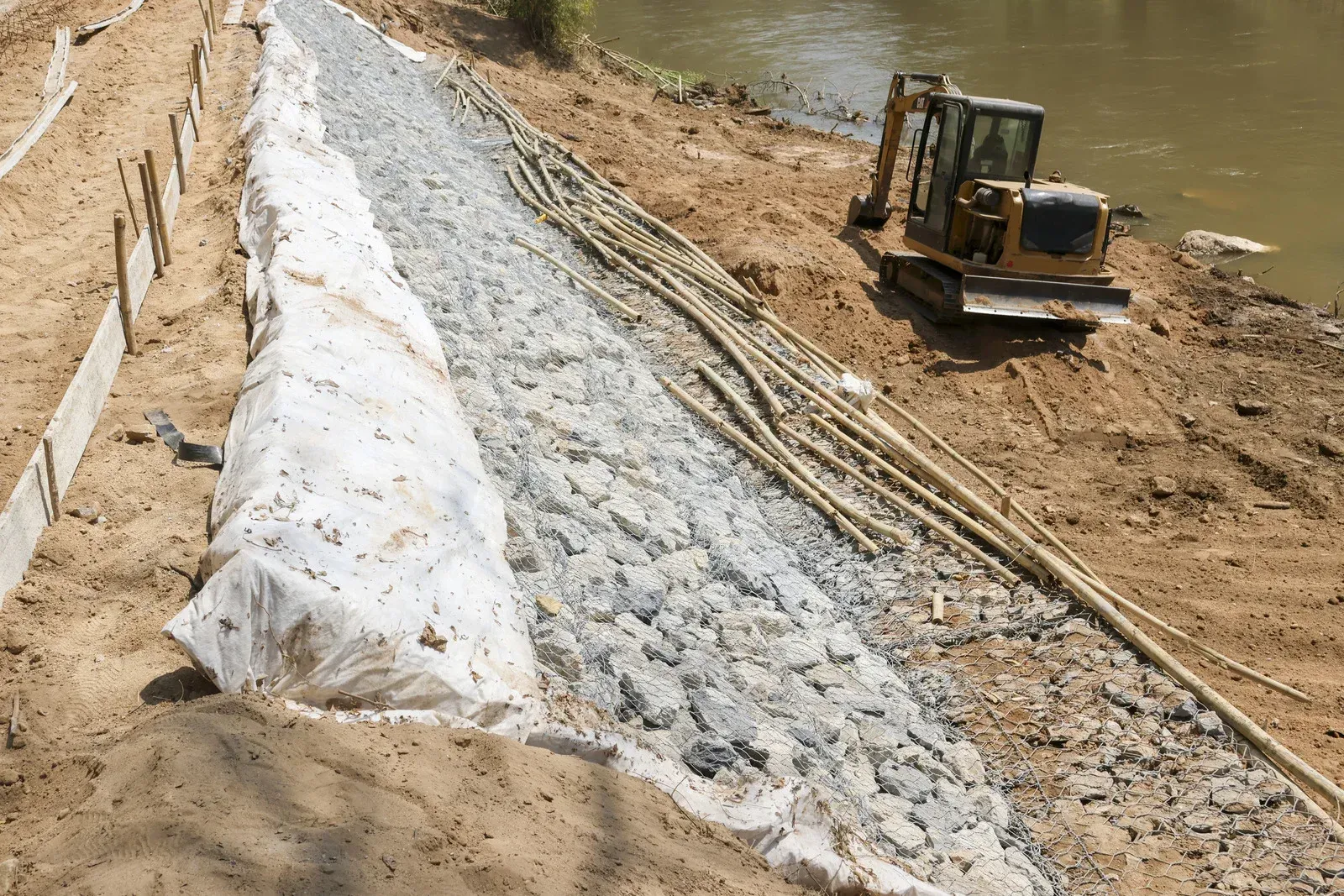 Construction site with excavator placing riprap along a riverbank slope