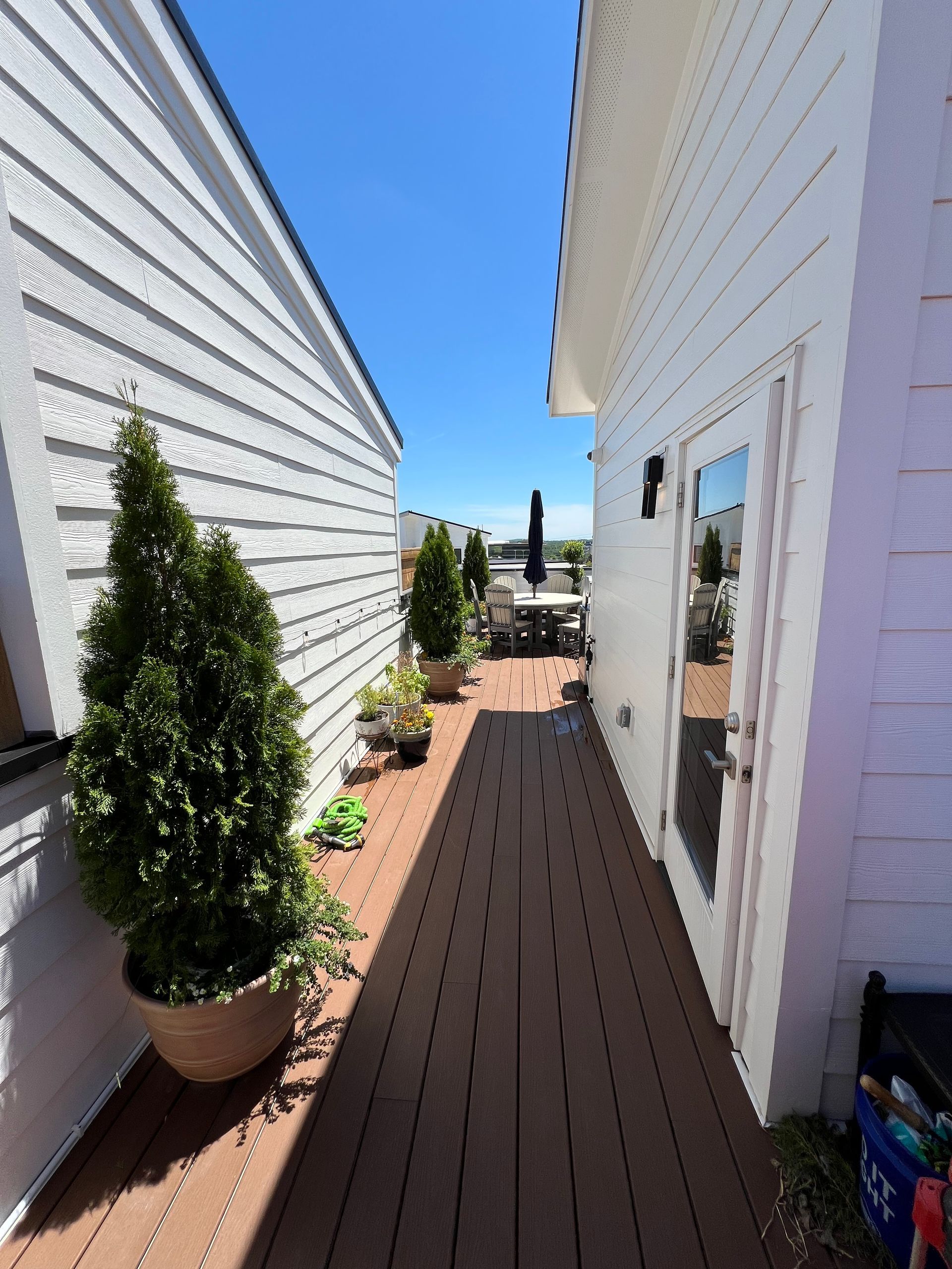 A wooden walkway between two buildings with potted plants on the side