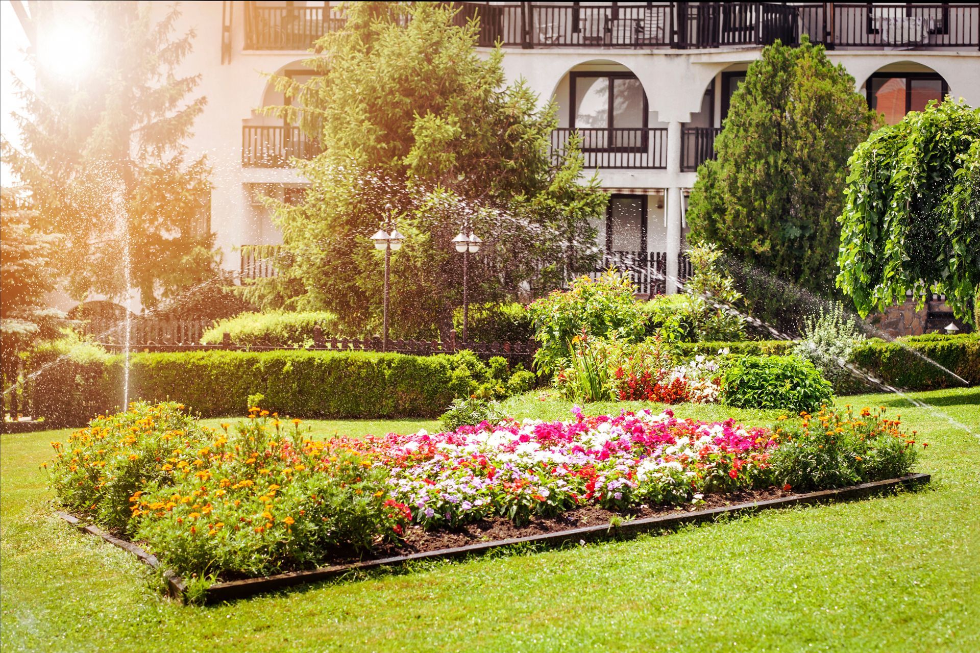 a garden with flowers and sprinklers in front of a building