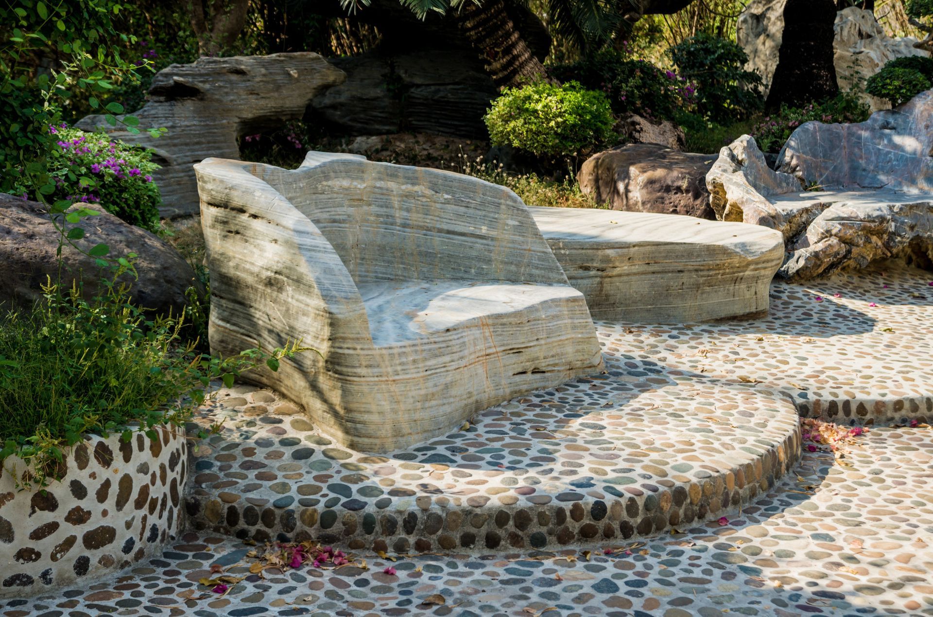 a stone bench is sitting on top of a stone walkway in a garden .