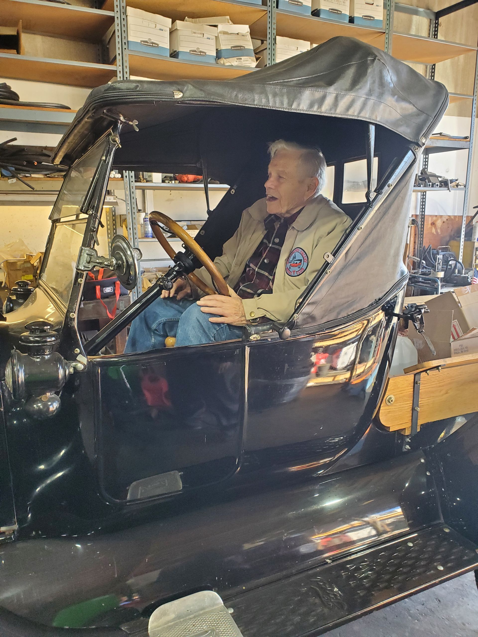 Elderly man in a vintage black car with a wood bed inside a garage. | Hal's Auto Care