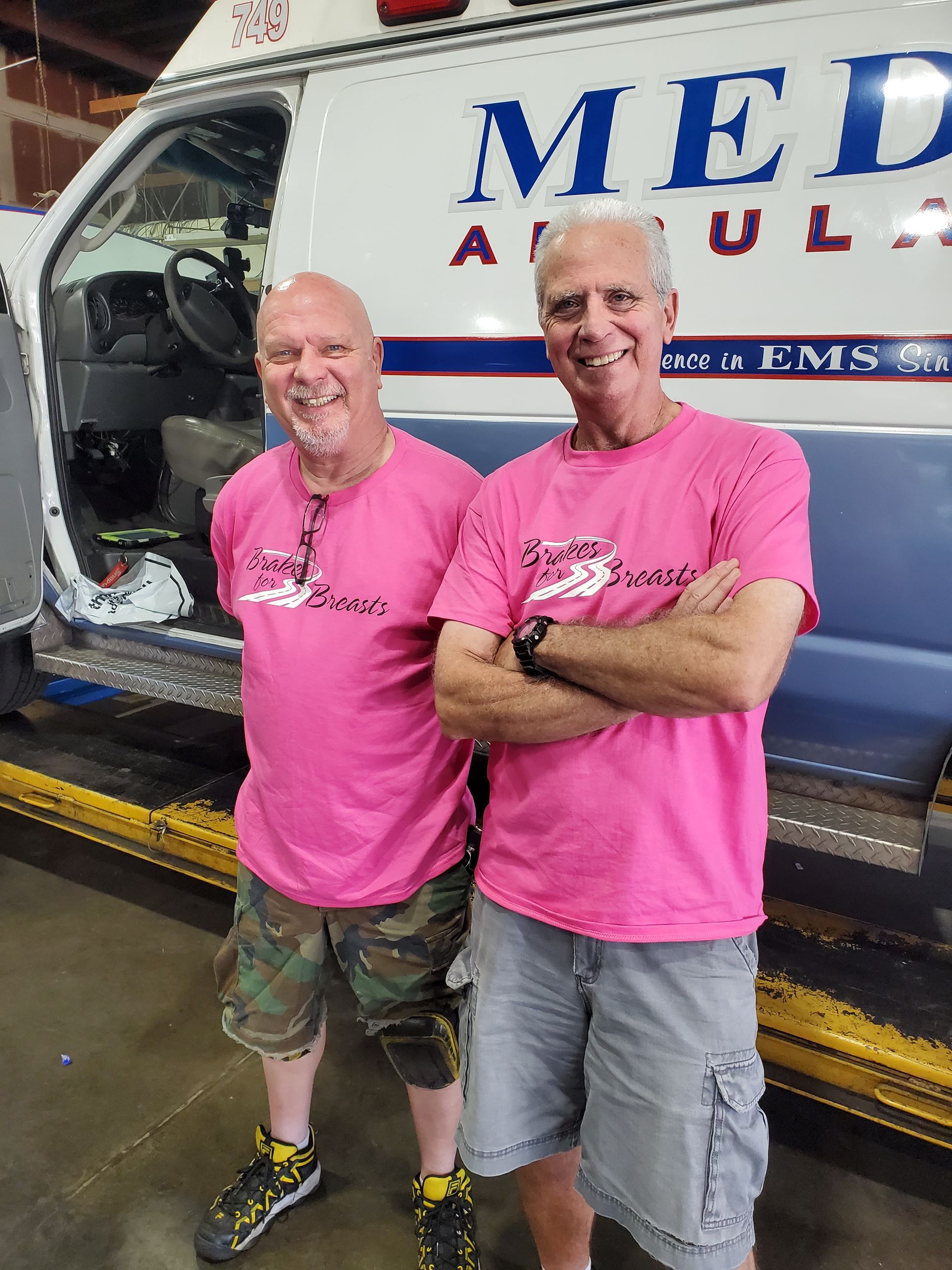 Two men in pink shirts stand by an ambulance. One has arms crossed, and the other has hands at his sides. | Hal's Auto Care