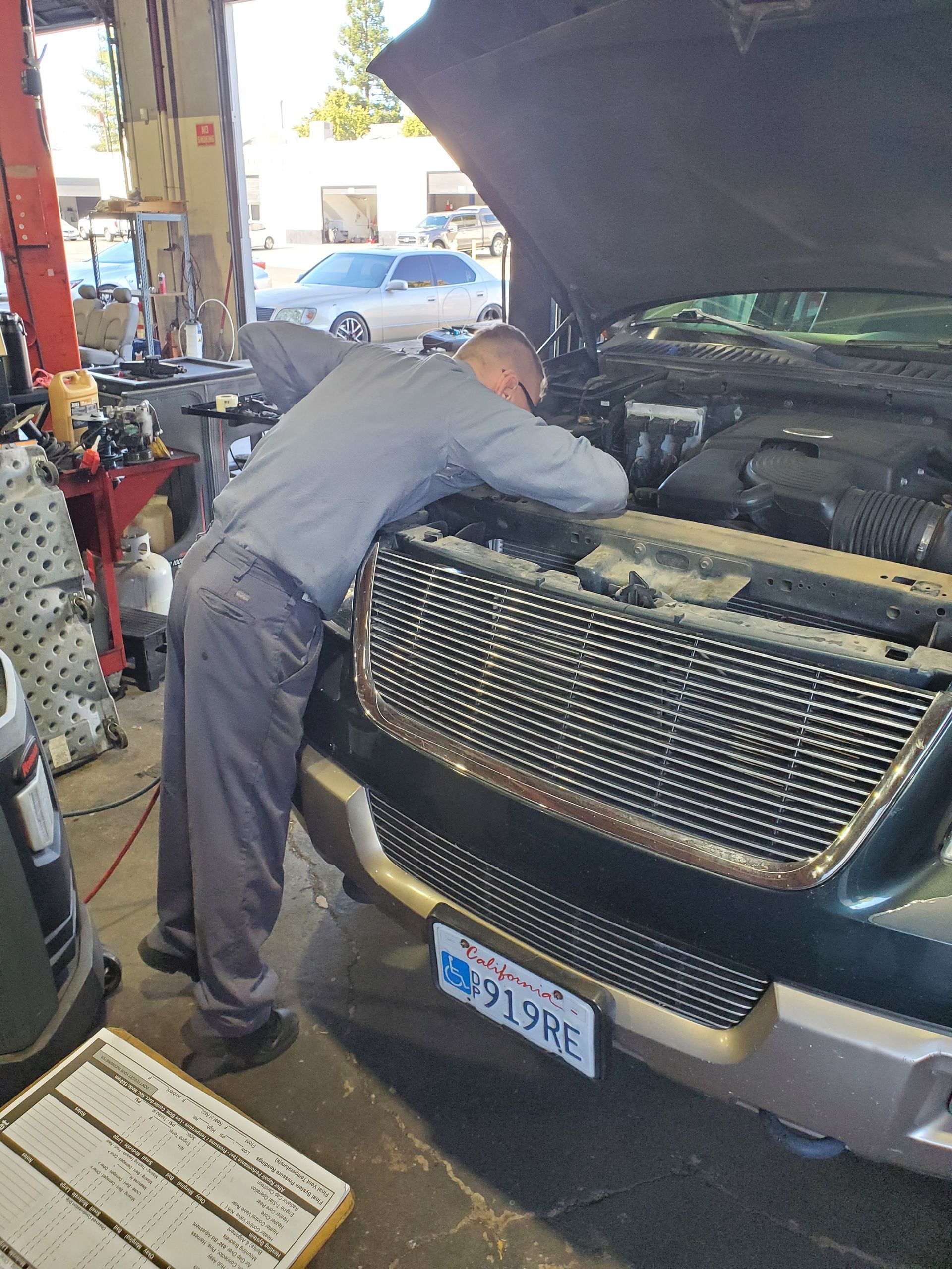 Mechanic working on a car engine in a garage, examining components. | Hal's Auto Care