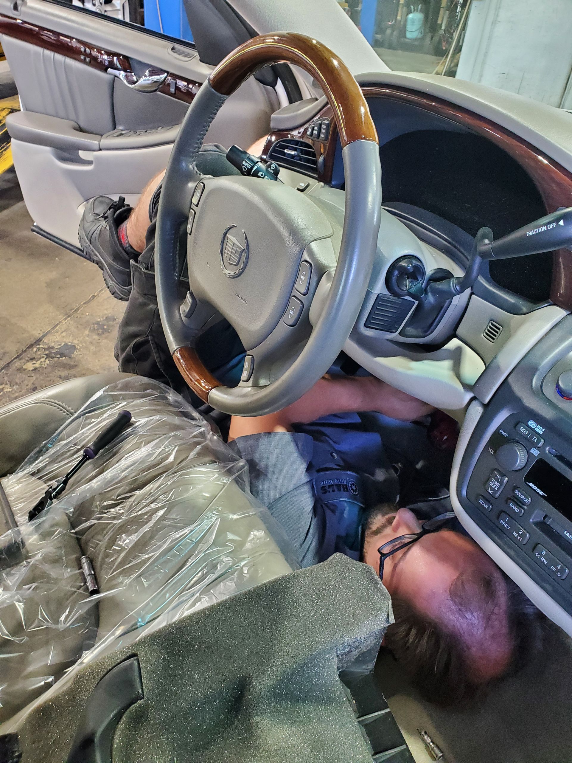 Person working under dashboard of tan Cadillac. Interior view, tools visible. | Hal's Auto Care
