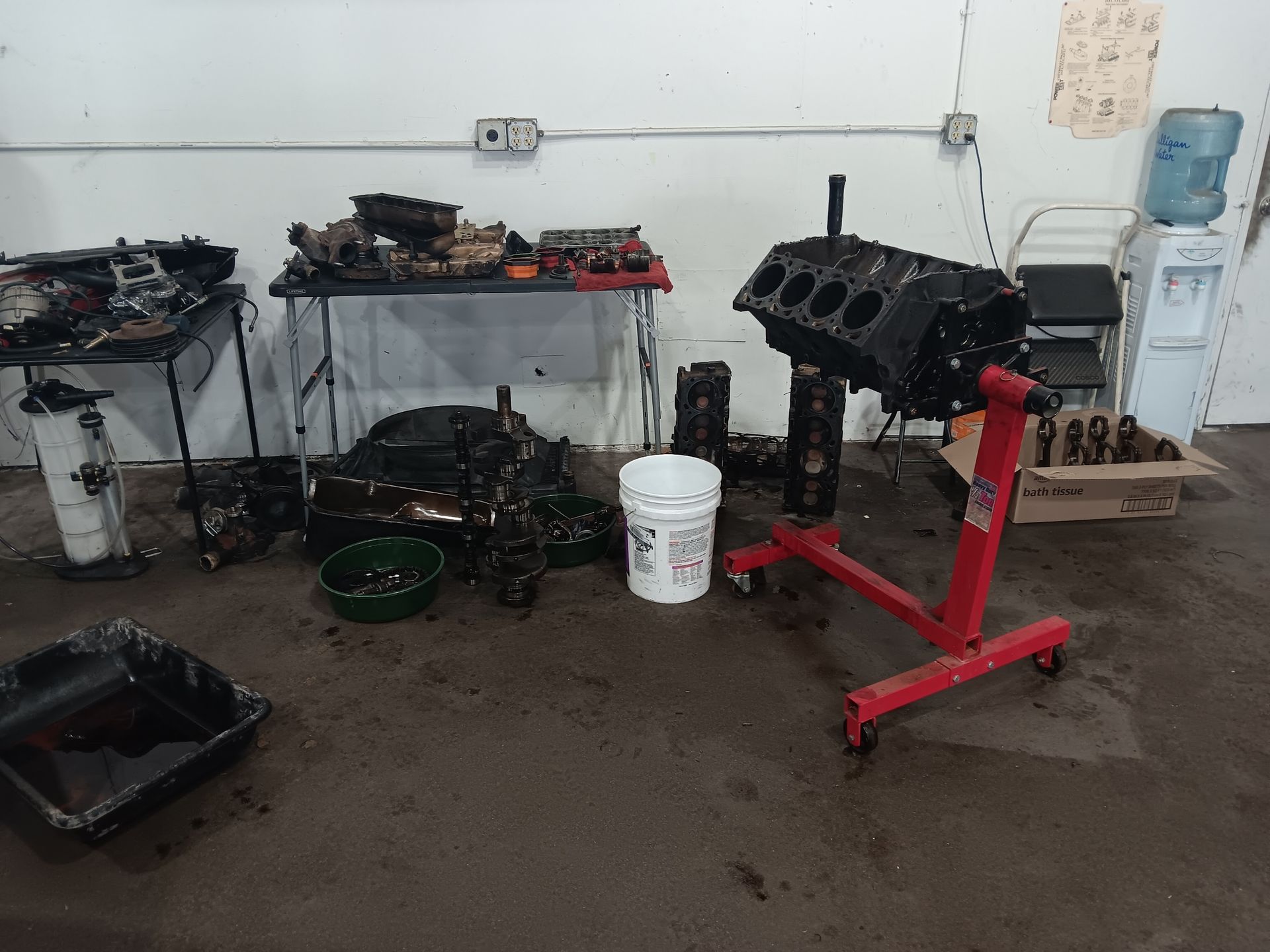 Engine parts scattered in a workshop, engine block on a stand, oily concrete floor. | Hal's Auto Care