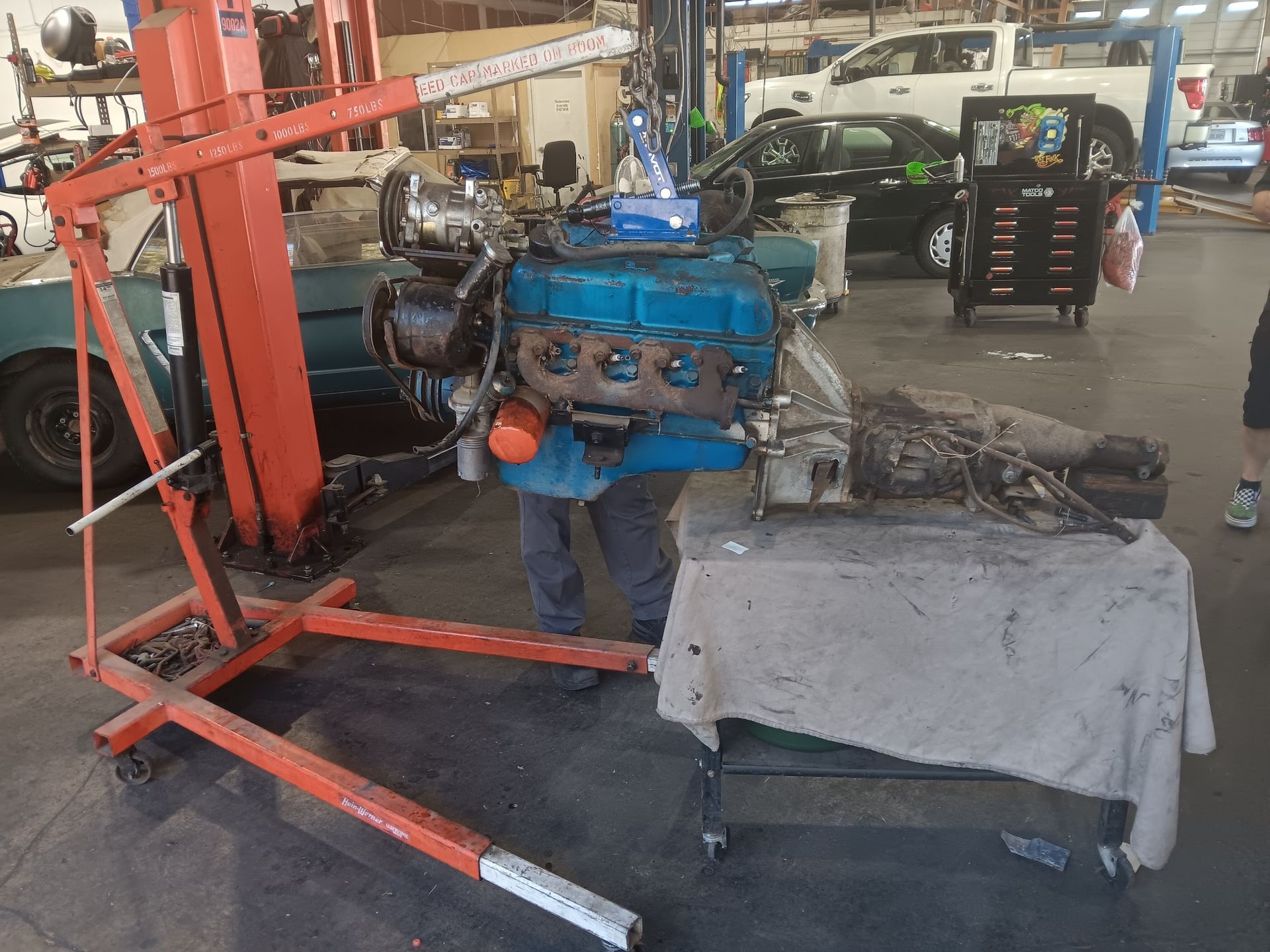 An engine supported by a lift in a garage. A person is working on it. | Hal's Auto Care
