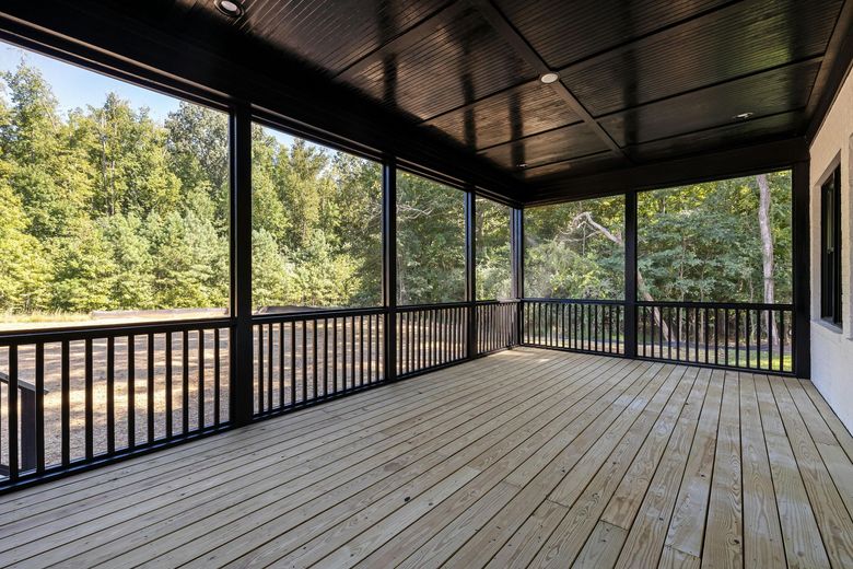 A screened in porch with a wooden deck and trees in the background.