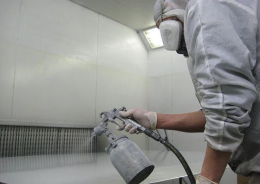 Person in protective gear spraying paint in a booth.
