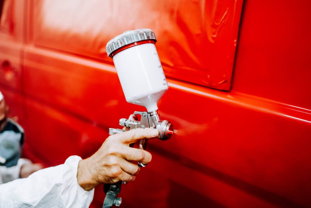 Person in blue gloves painting car with spray gun in a paint booth.