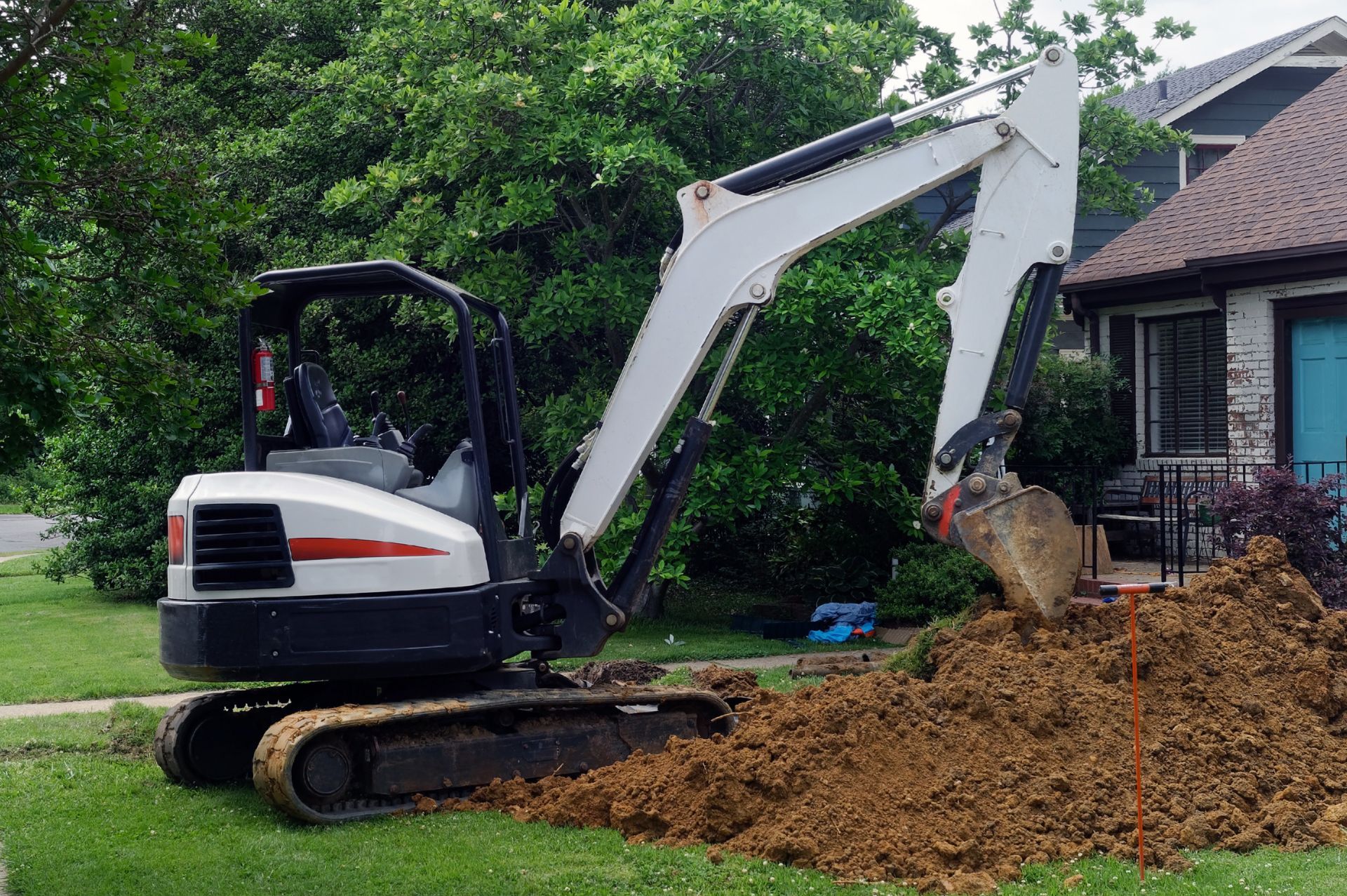 Mini excavator digging dirt near a house on a green lawn.