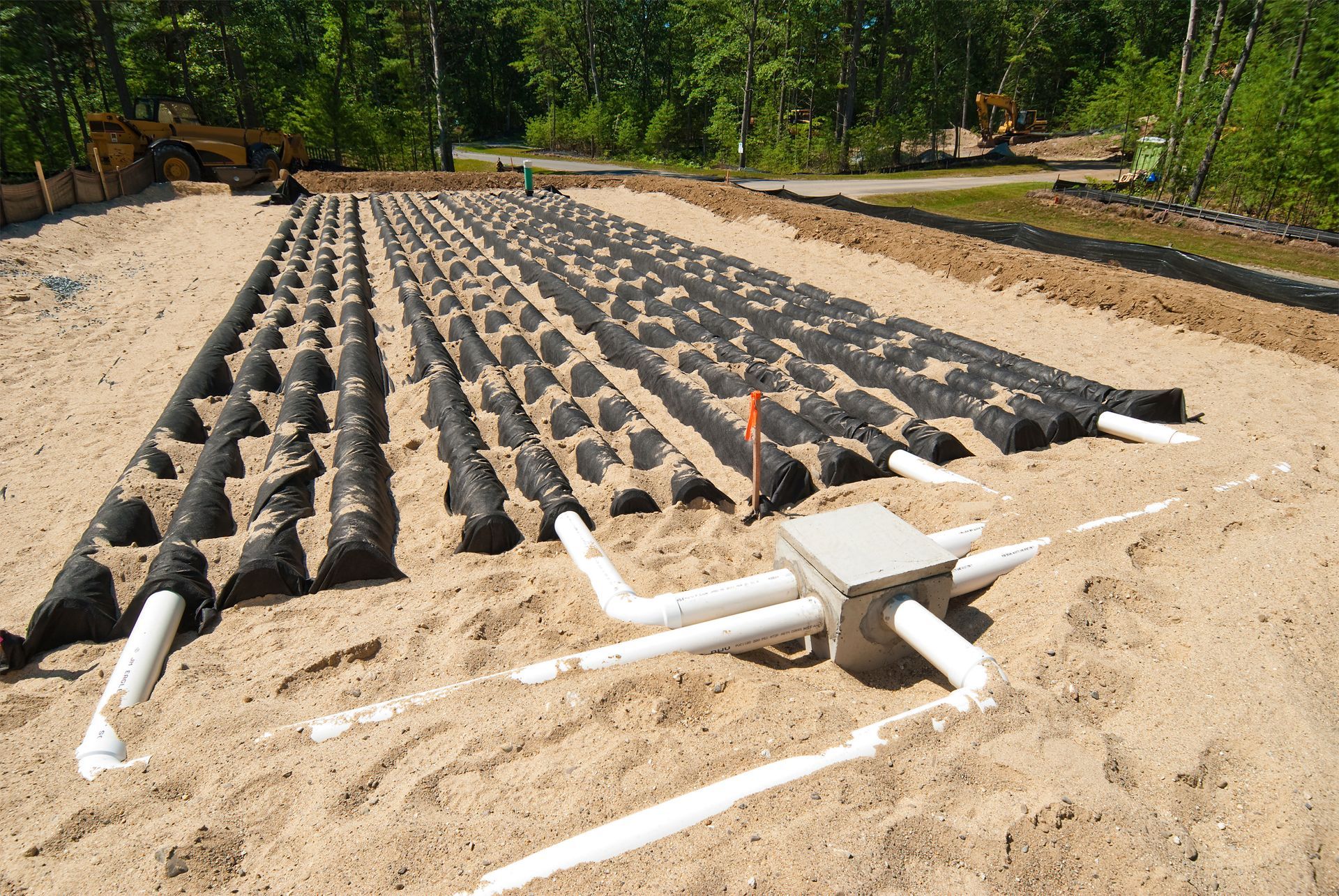 Septic system field with black drainfield media, white pipes, and a concrete distribution box in sand.