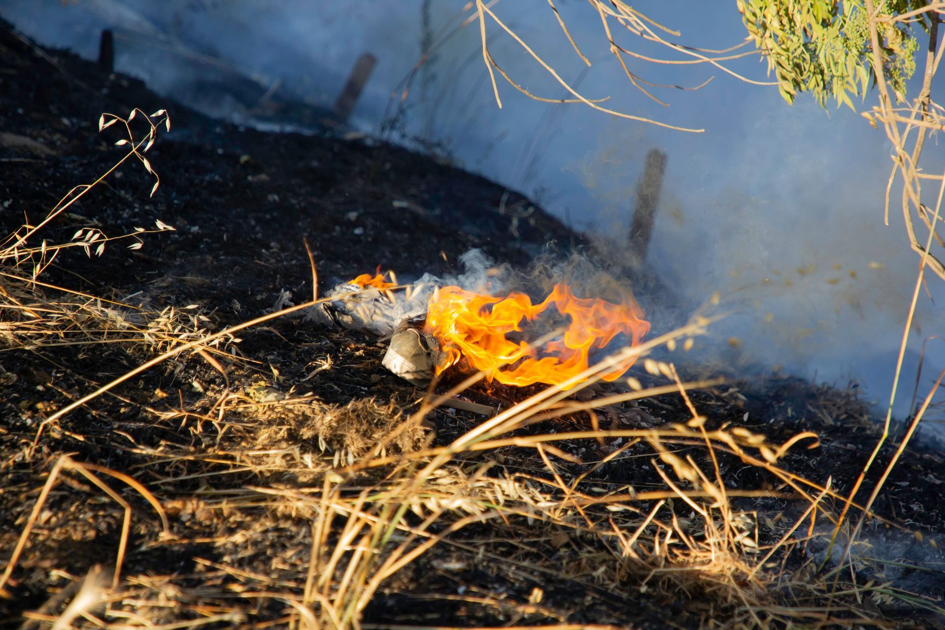 Fire burning in dry grass on a hillside, with smoke rising.