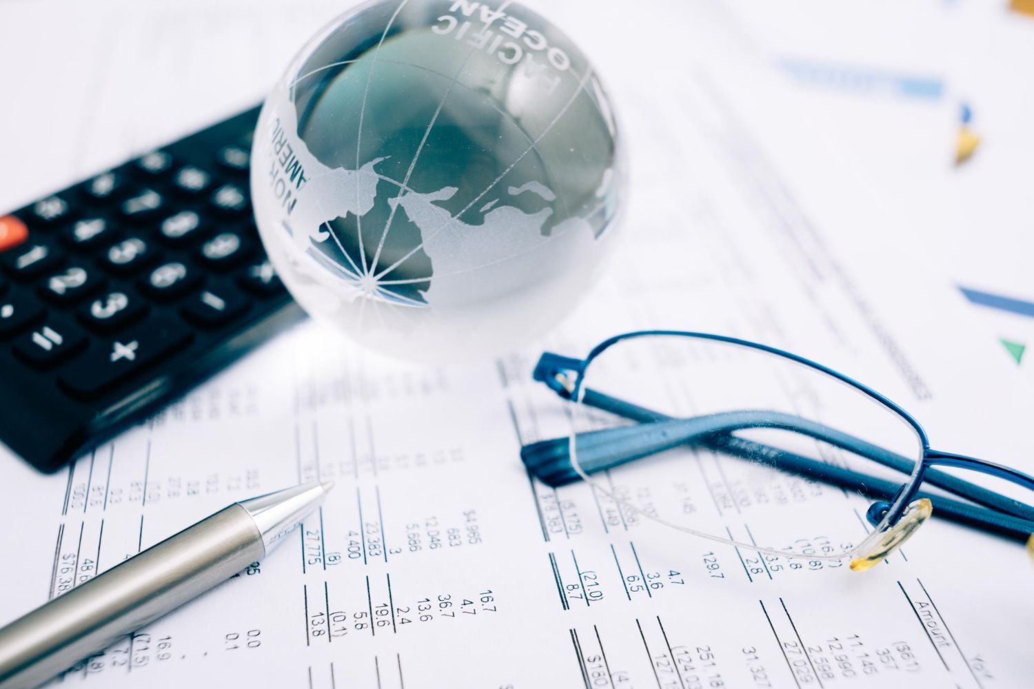 Calculadora, globo, óculos e caneta em documentos financeiros.