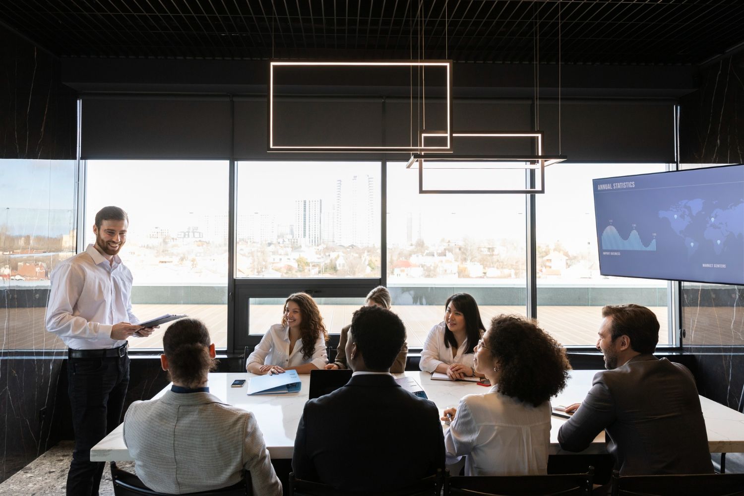Homem faz apresentação para colegas em volta de uma mesa em um escritório moderno; quadro branco, vista da cidade.