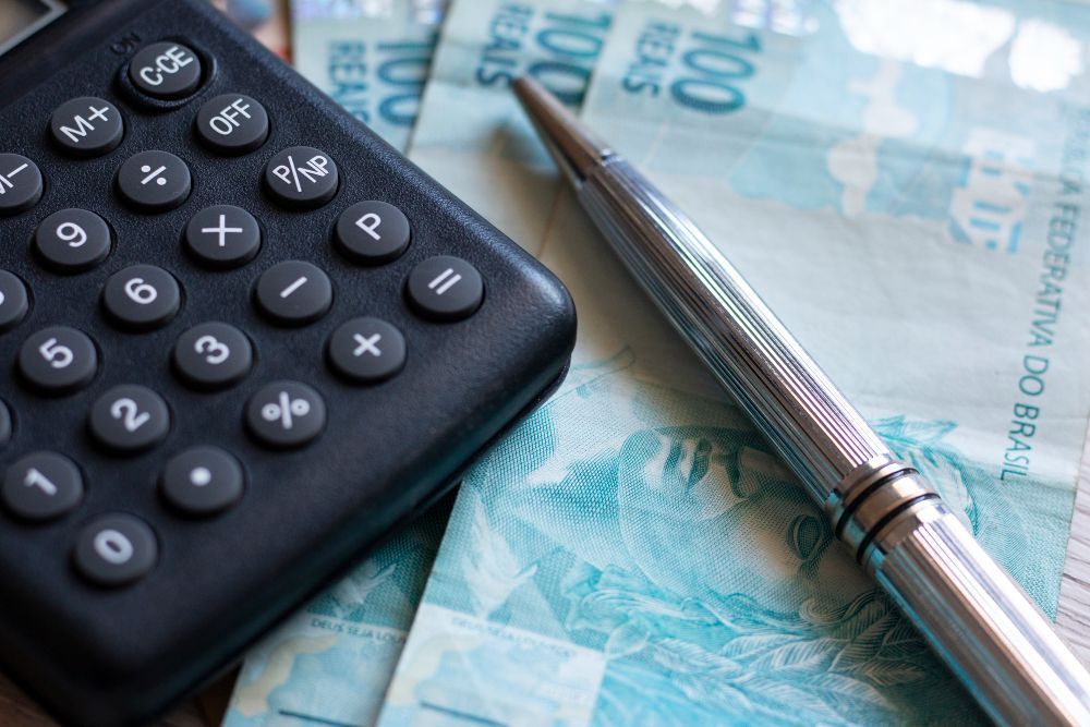 Calculadora, caneta e notas de real brasileiro, sugerindo planejamento financeiro.