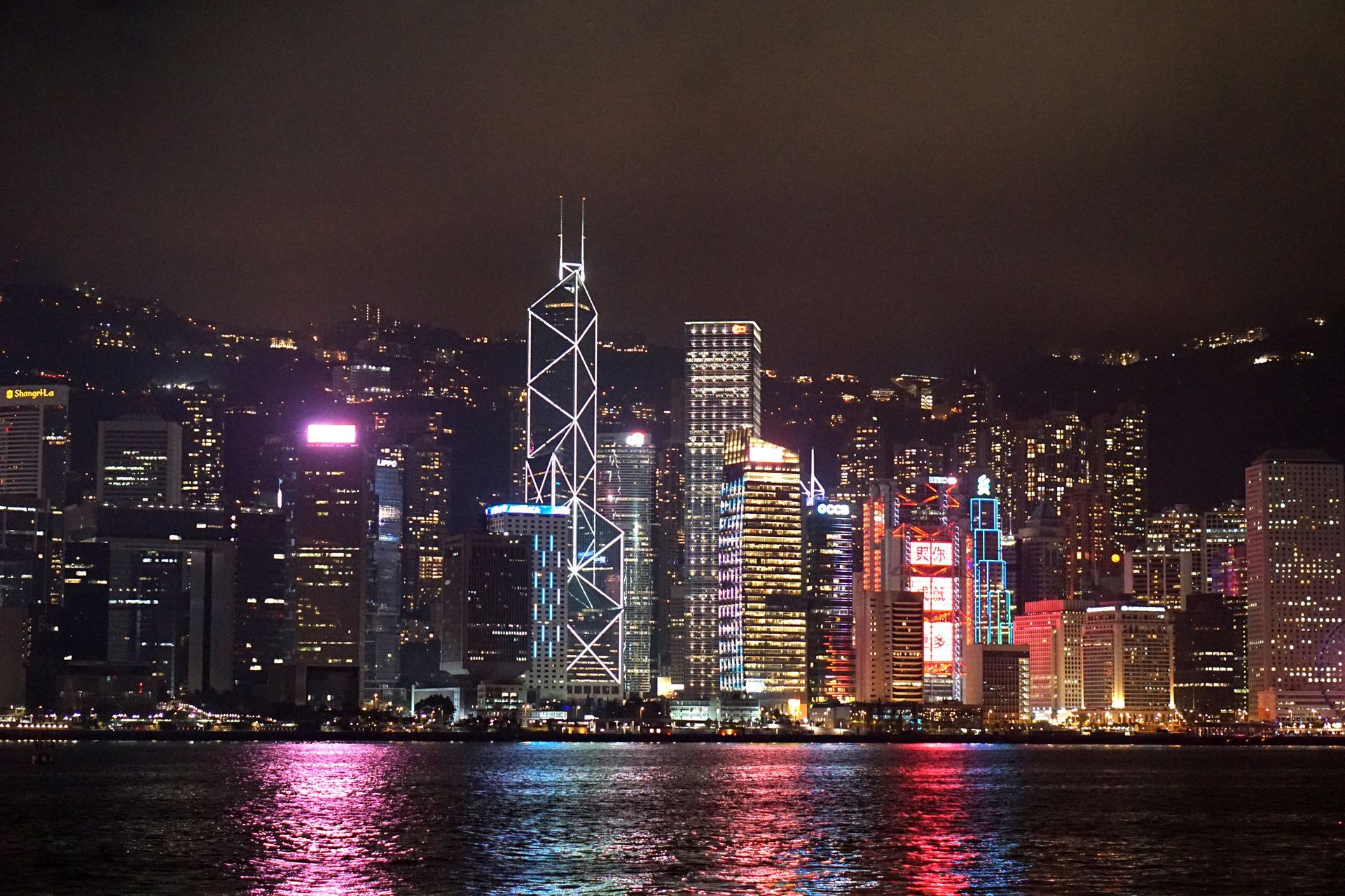 Vista noturna do horizonte de Hong Kong com arranha-céus iluminados e água em primeiro plano.