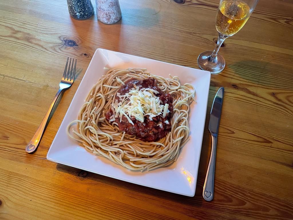 A plate of spaghetti with sauce and cheese on a wooden table.