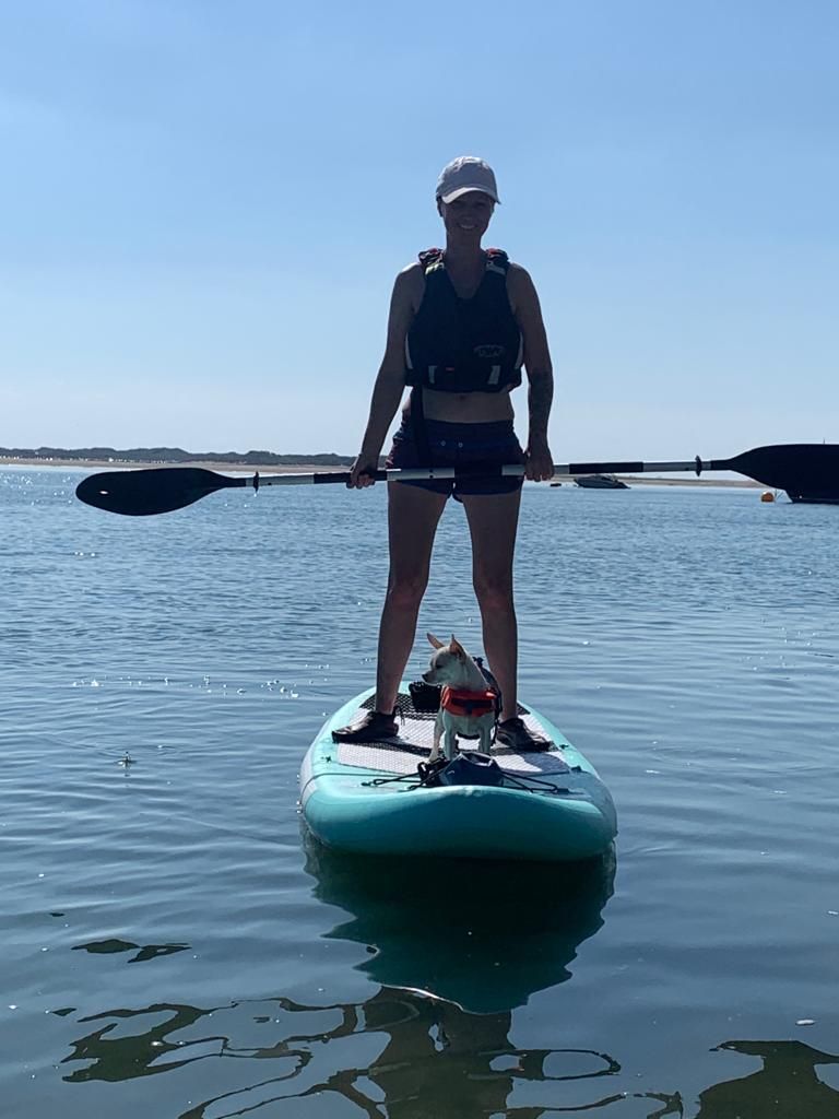 A woman is standing on a paddle board with a dog.