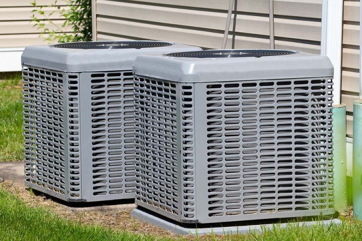 Two air conditioners are sitting in the grass in front of a house.