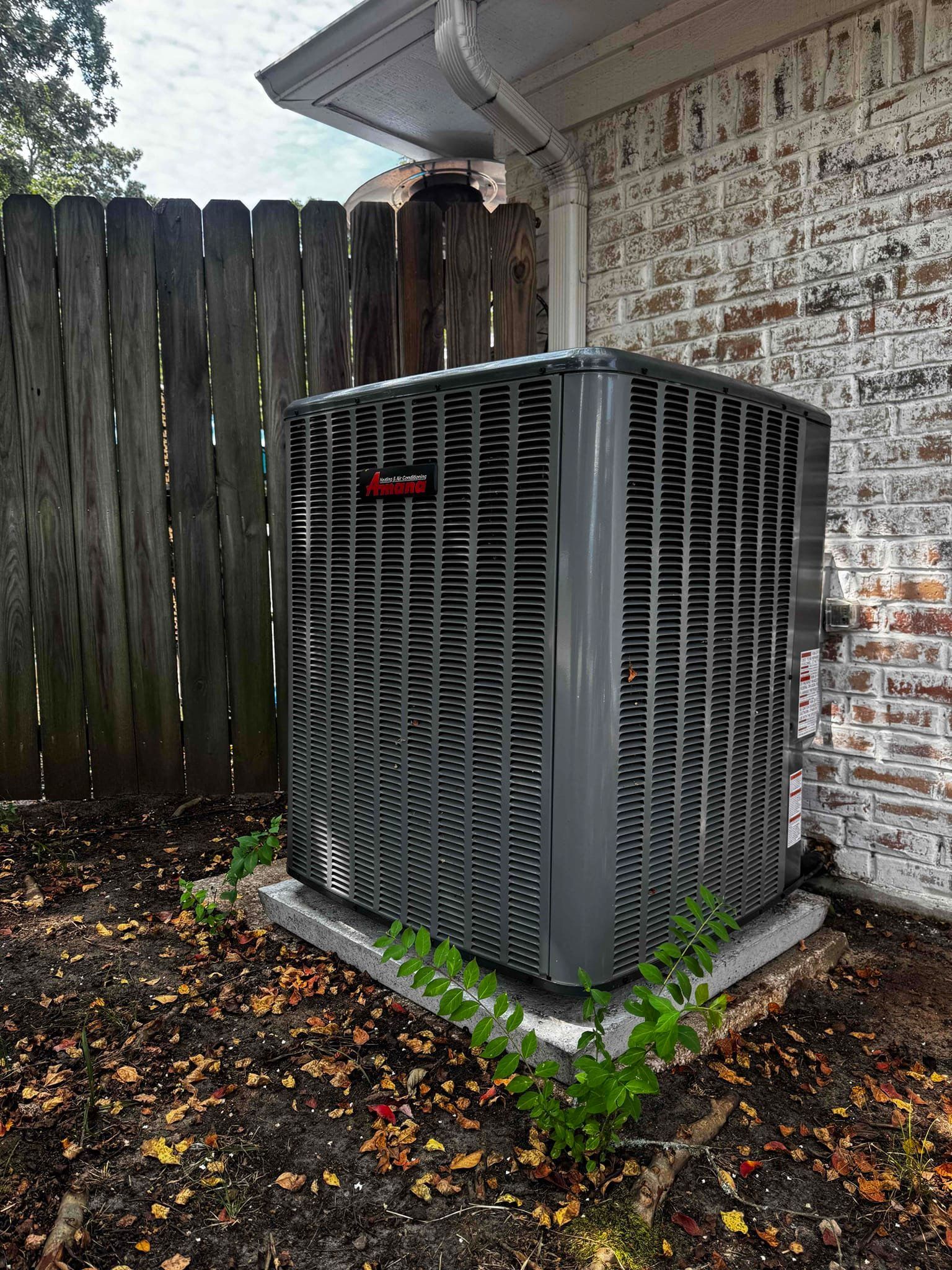 Two men are looking at a fan on the side of a building.