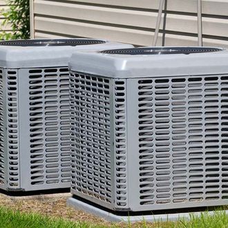 Two air conditioners are sitting next to each other in a yard.