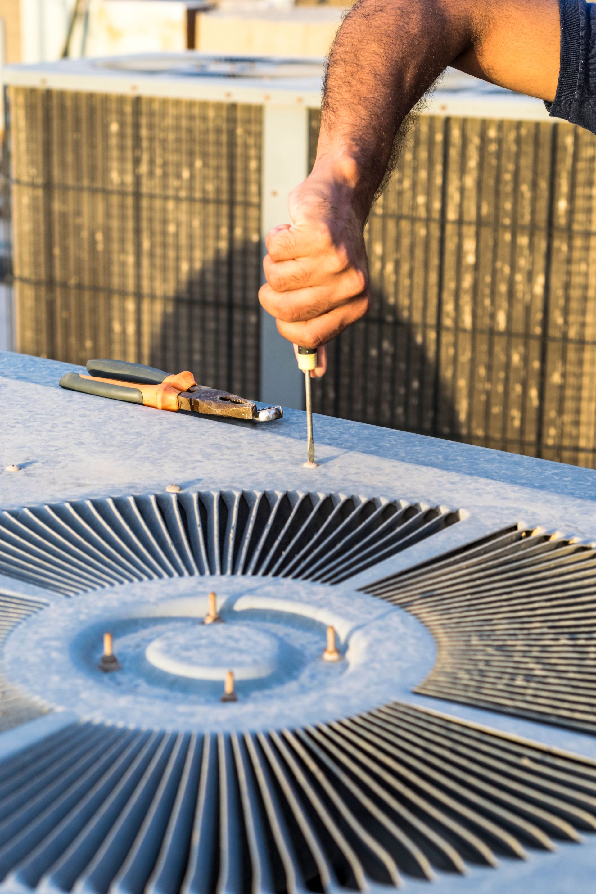 A man is fixing an air conditioner with a screwdriver.