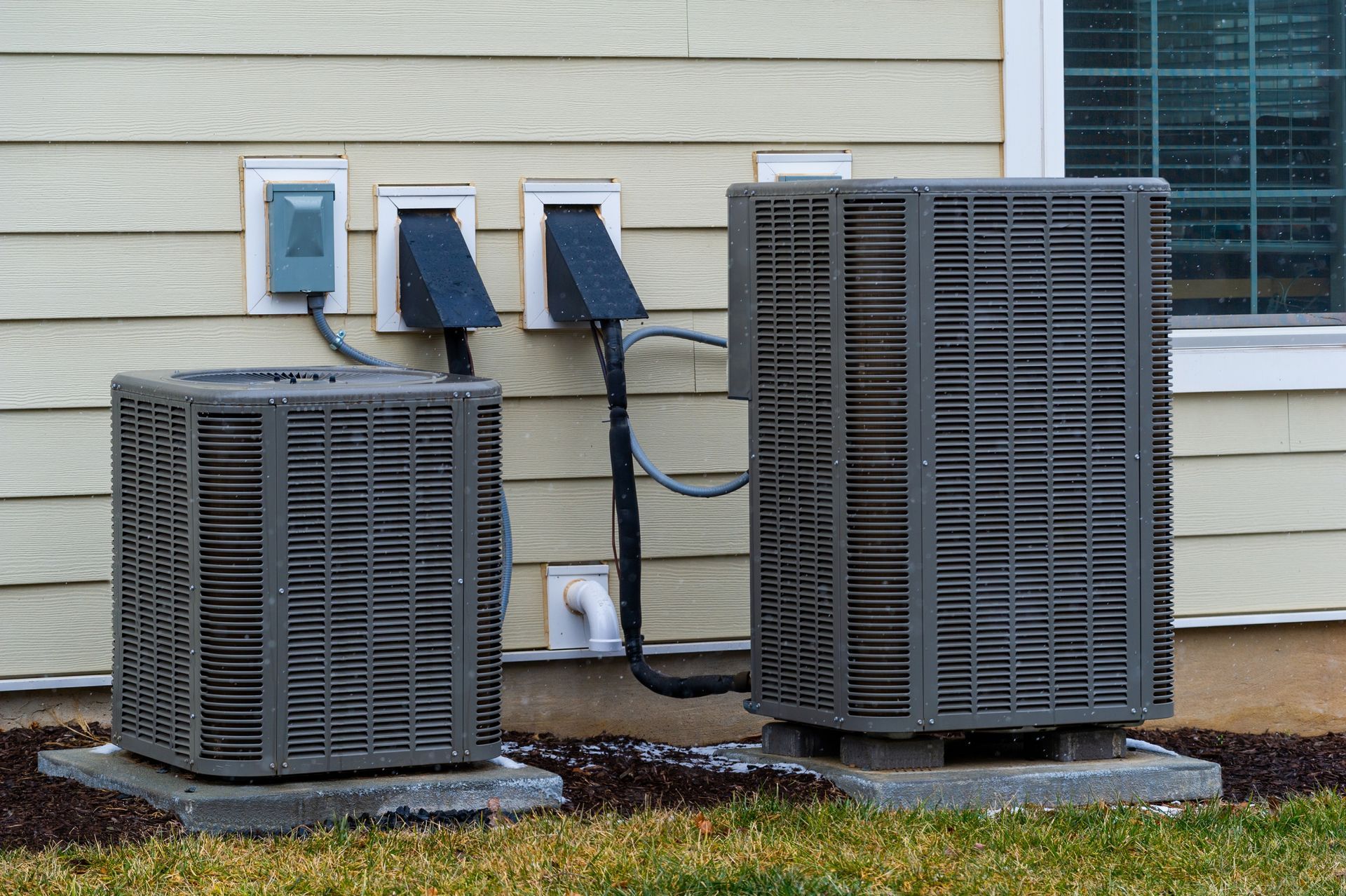 Two air conditioners are sitting outside of a house.