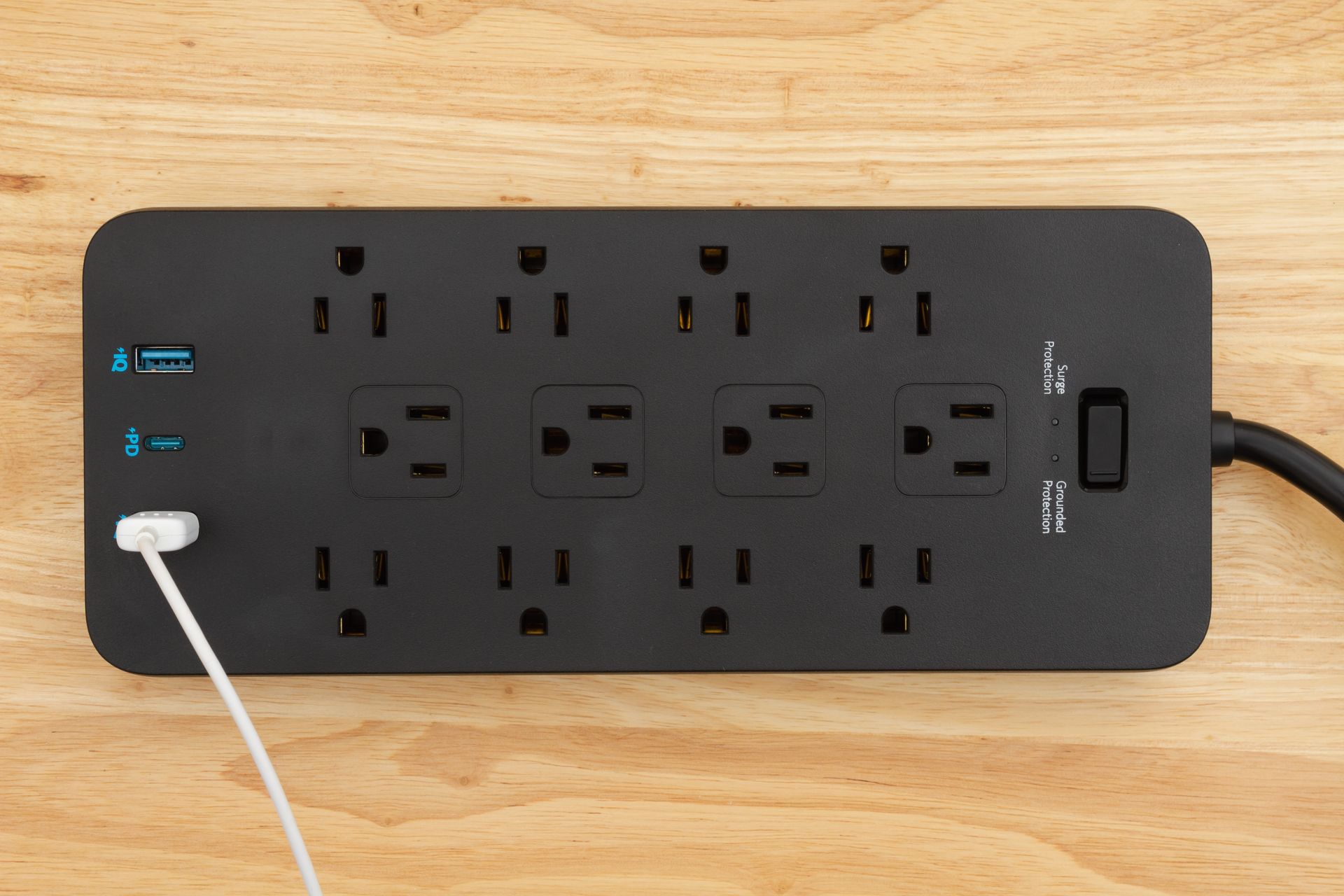 A power strip is sitting on a wooden table with a cord plugged into it.