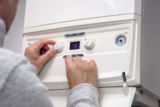 Person adjusting the knobs on a white boiler, likely setting the heating.