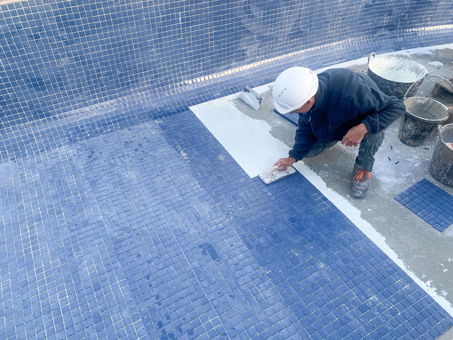 A man is laying tiles on the floor of a swimming pool.