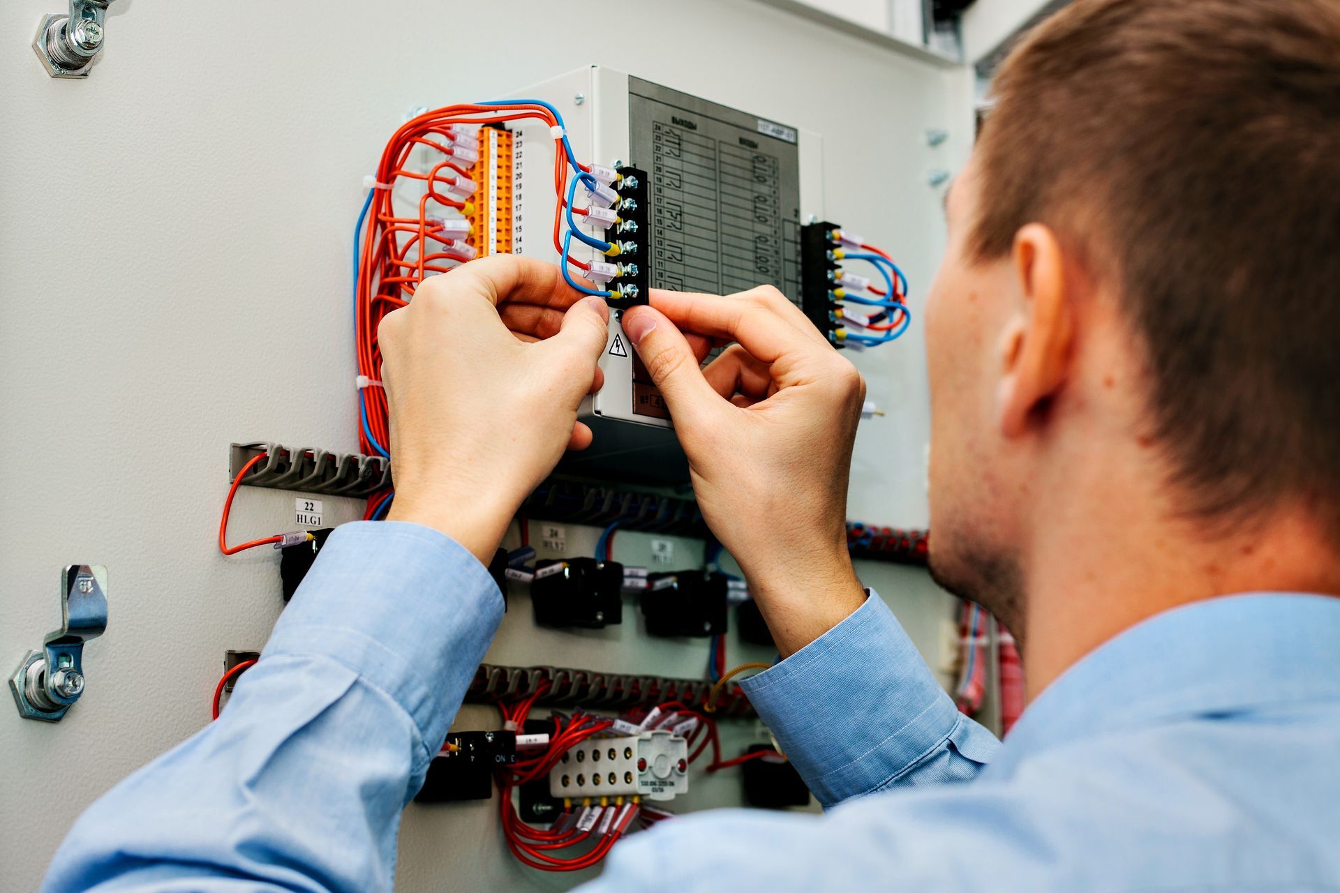 A man in a blue shirt is working on an electrical box.