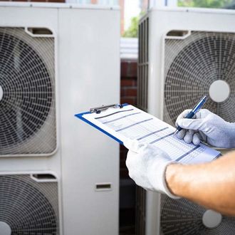 A person is writing on a clipboard in front of air conditioners.