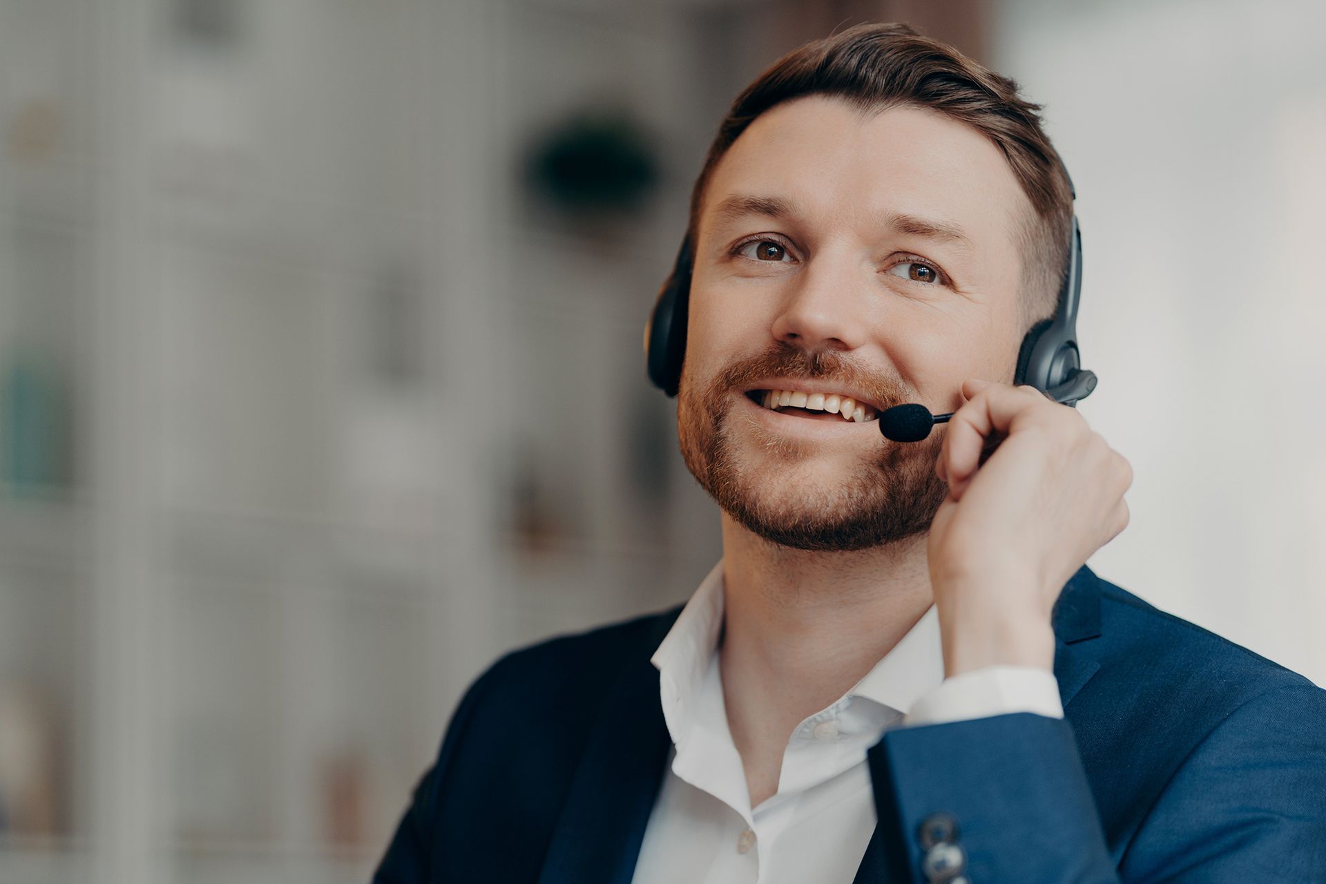 A man in a suit is wearing a headset and smiling.