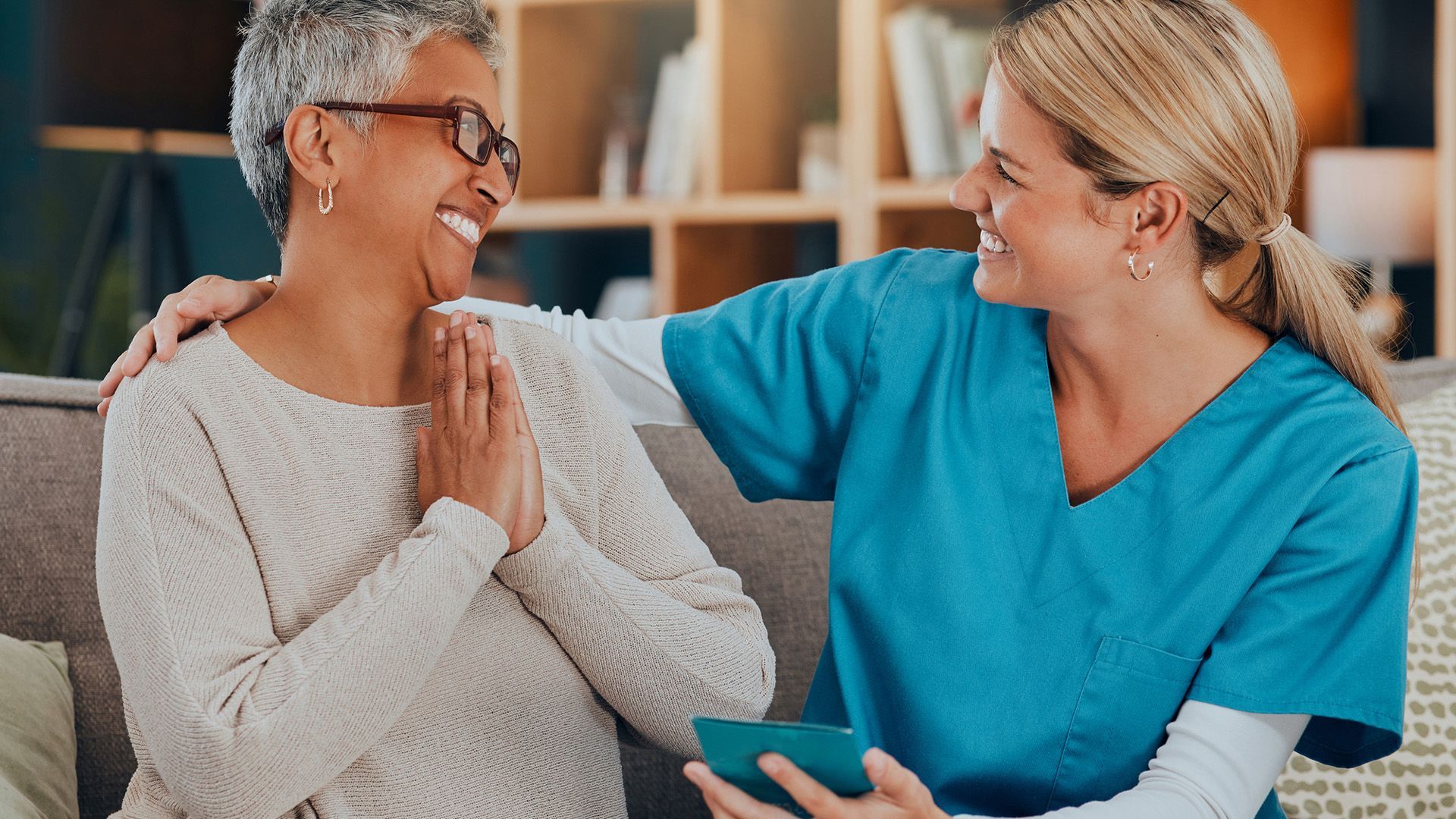 A nurse is talking to an elderly woman on a couch.