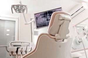 A dental chair in a dental office with a monitor above it.
