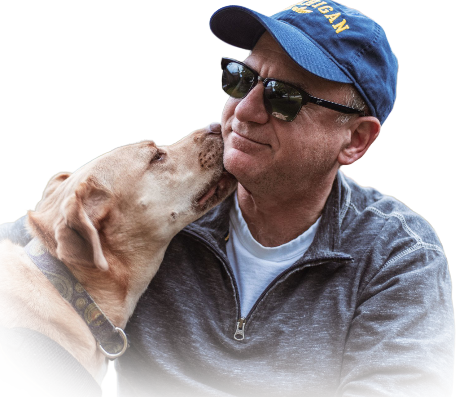 A person wearing a blue baseball cap and sunglasses is being affectionately licked on the cheek by a light-colored dog.