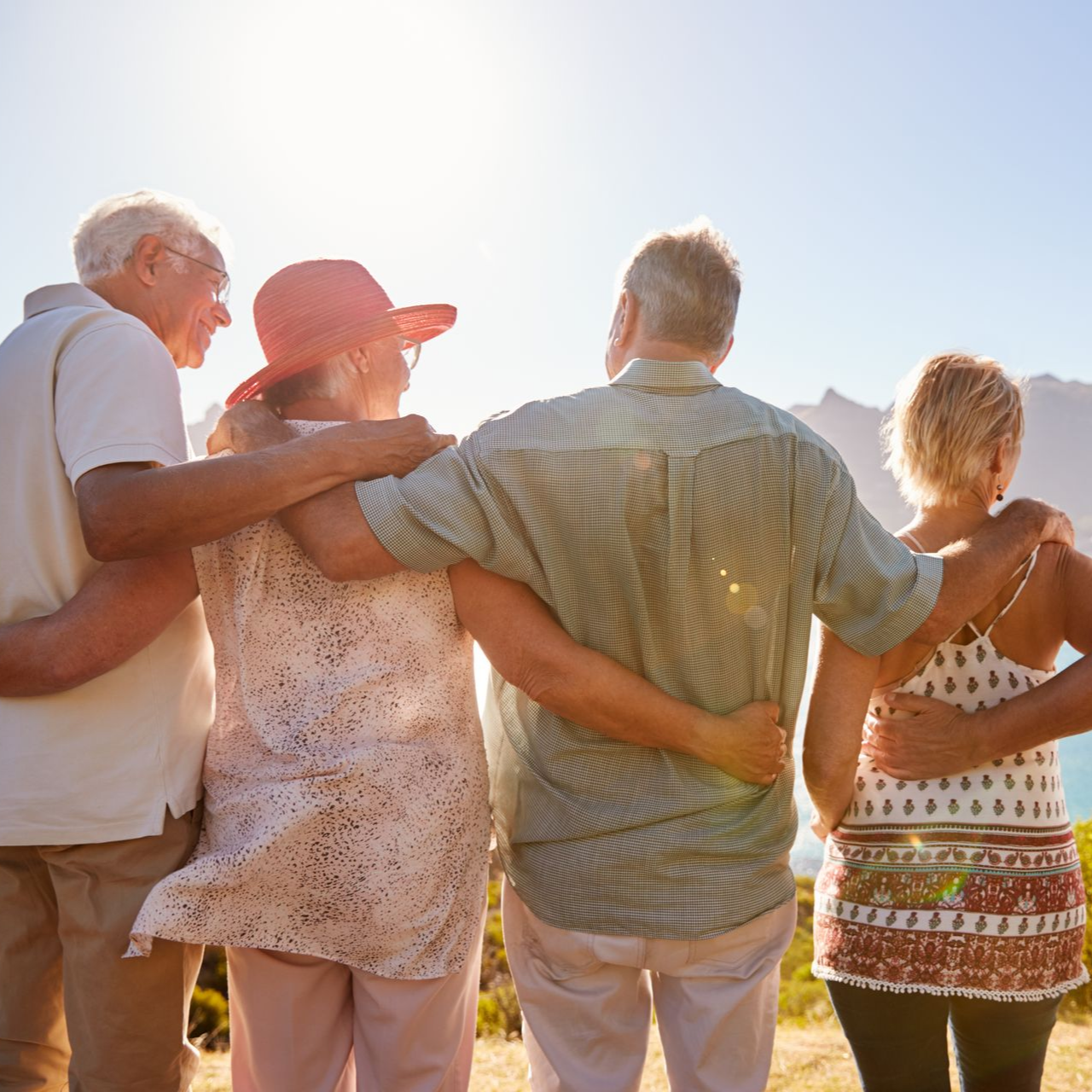 A couple wrapped in a grey blanket sitting in a forest setting, with the person on the left kissing the other's forehead.