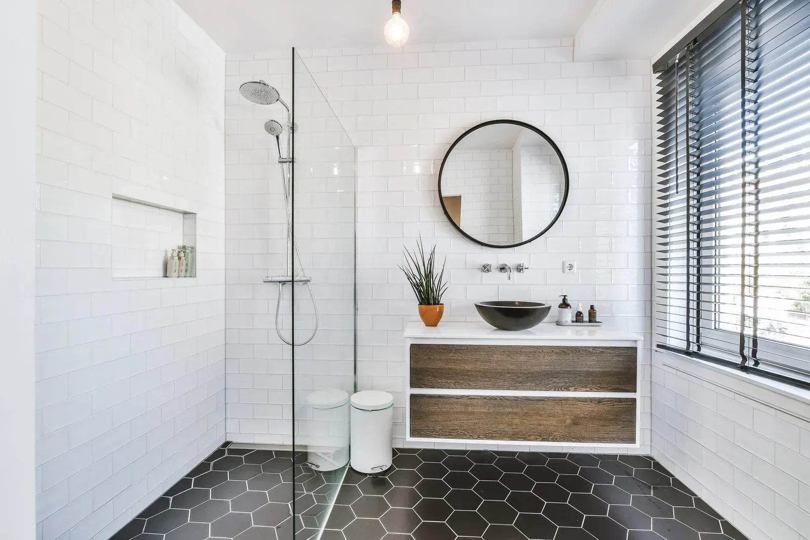 Modern bathroom with a glass shower, dark hexagon floor, and white subway tile walls.
