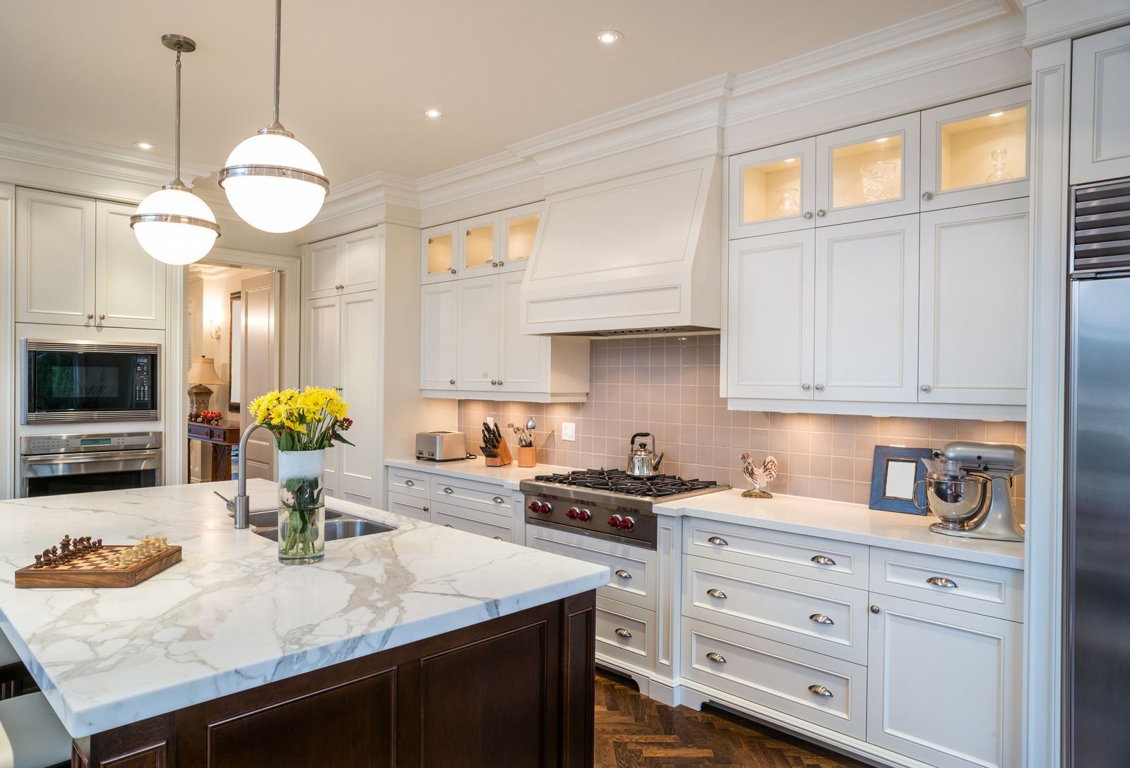 White kitchen with marble island, range, and cabinetry; warm lighting, floral centerpiece.