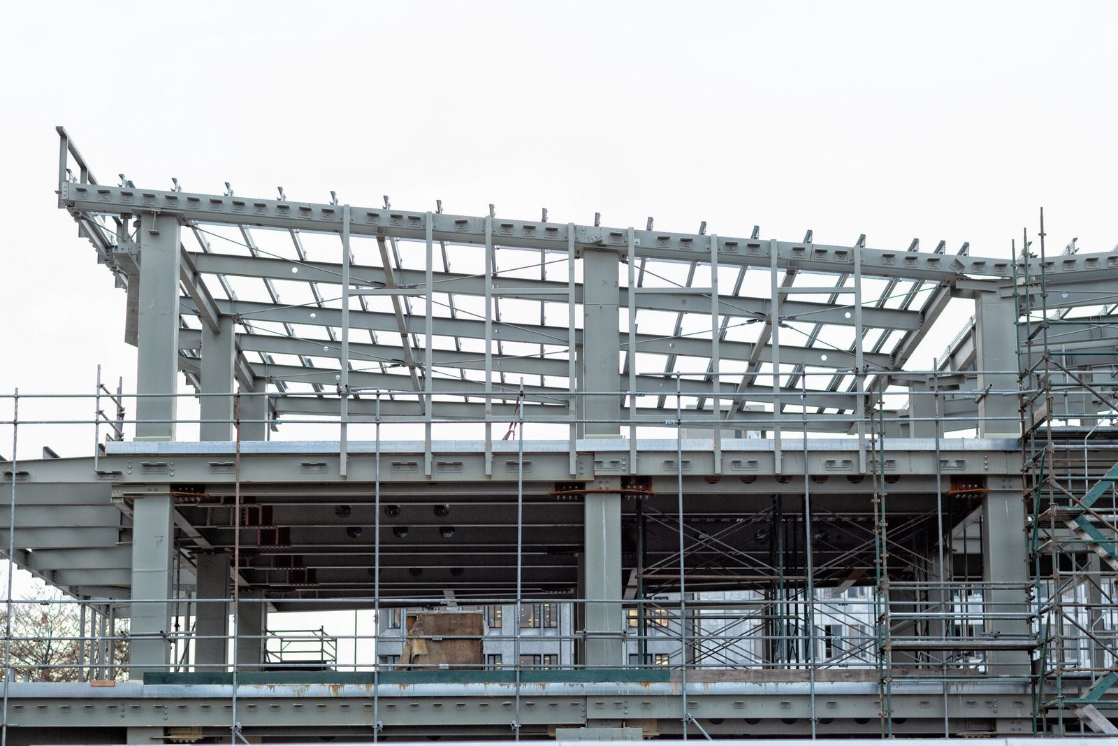 Steel frame of a building under construction, with scaffolding around the structure and overcast sky in the background.