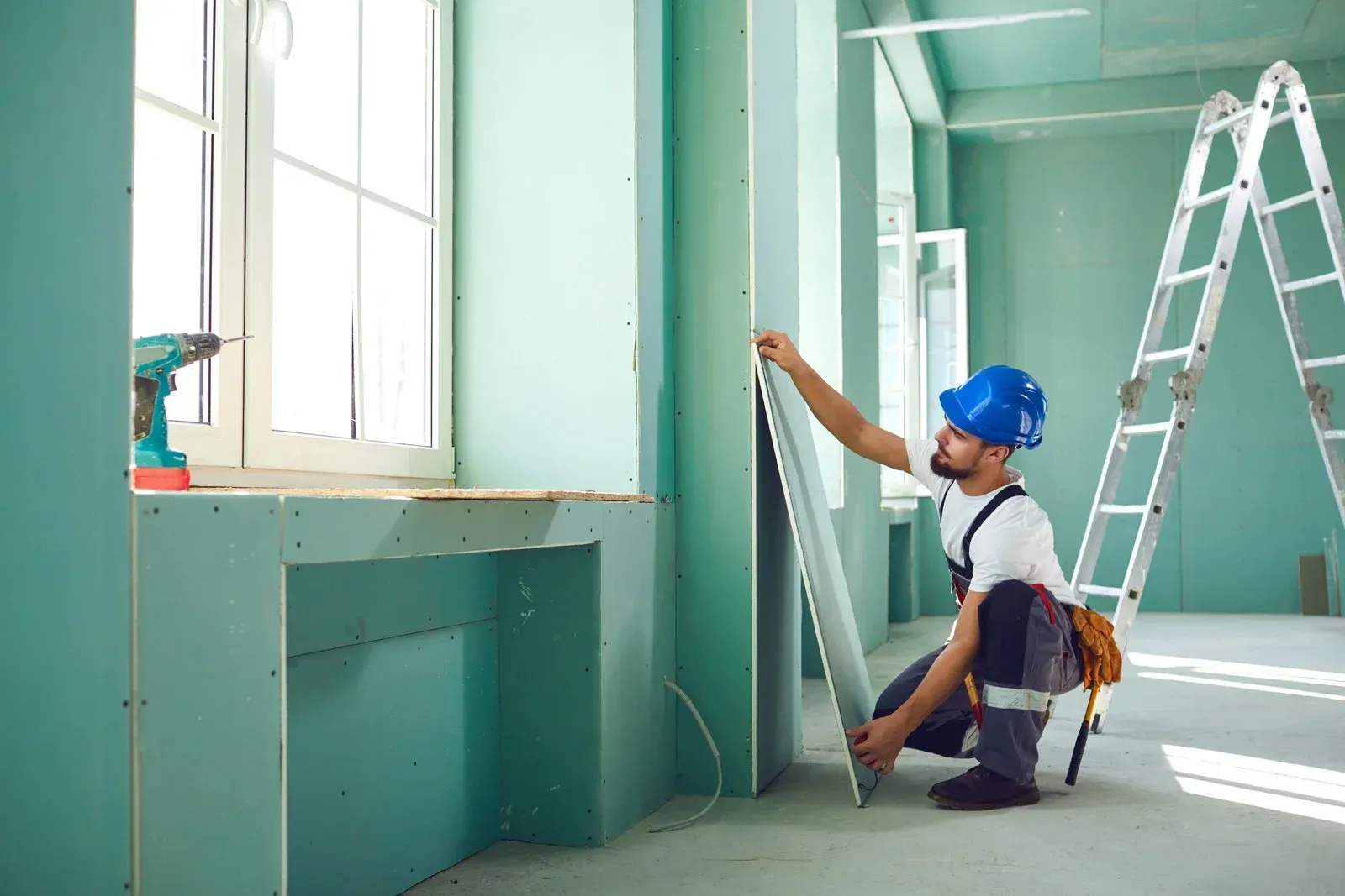 A man is measuring a piece of drywall in an empty room.