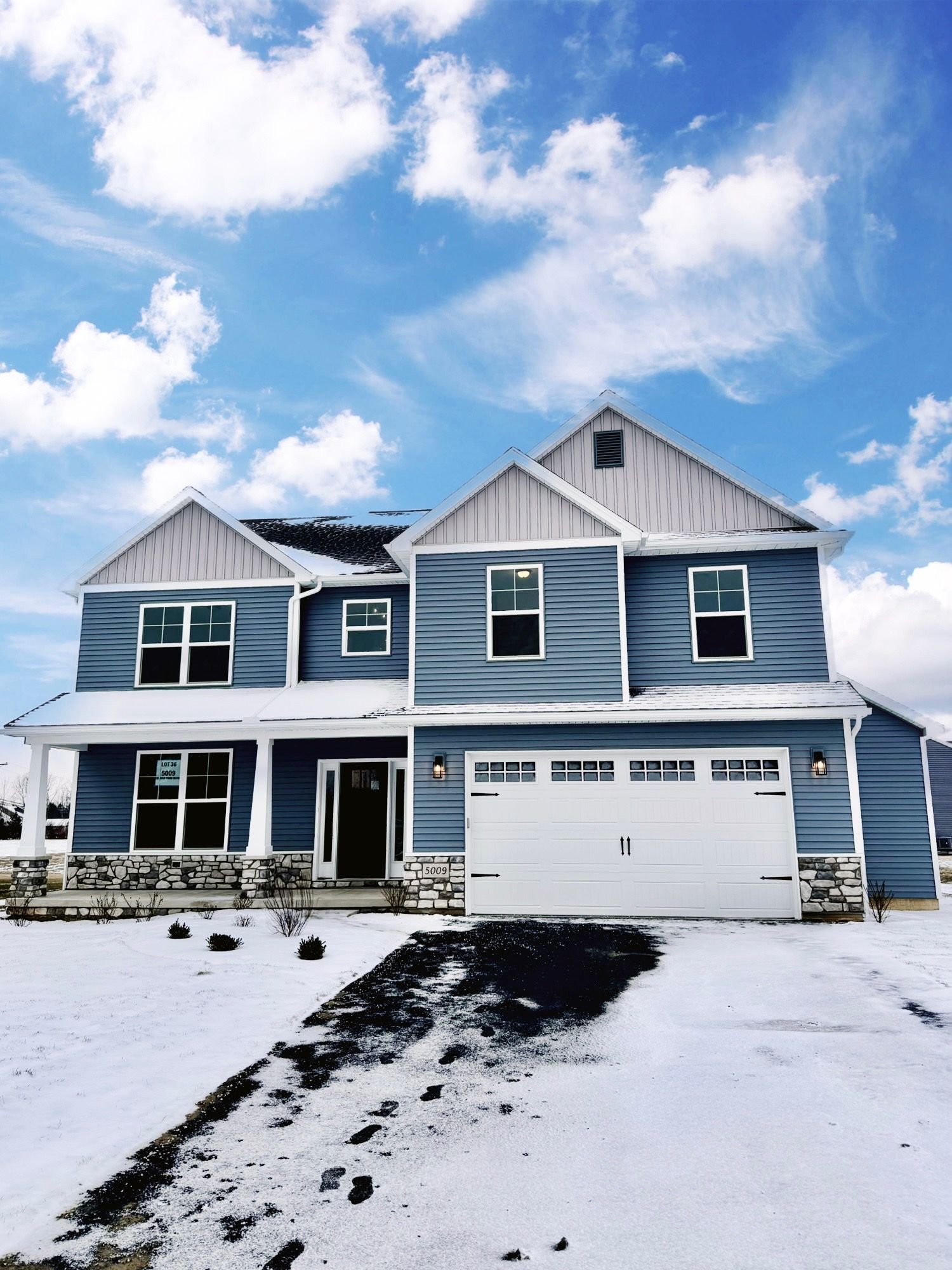 A blue house with a white garage door is covered in snow