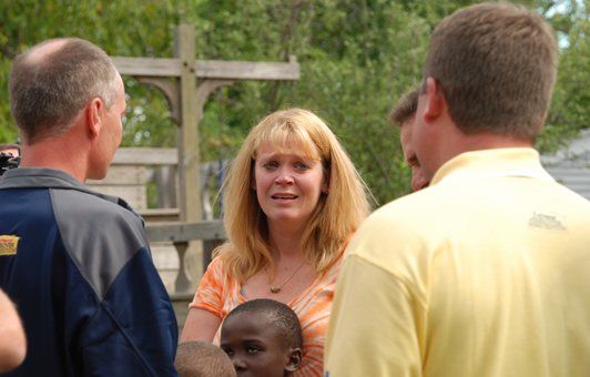 A group of people are standing around a woman holding a baby.