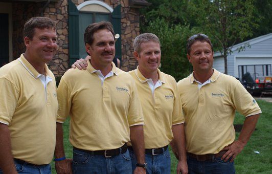 Four men are posing for a picture in front of a house