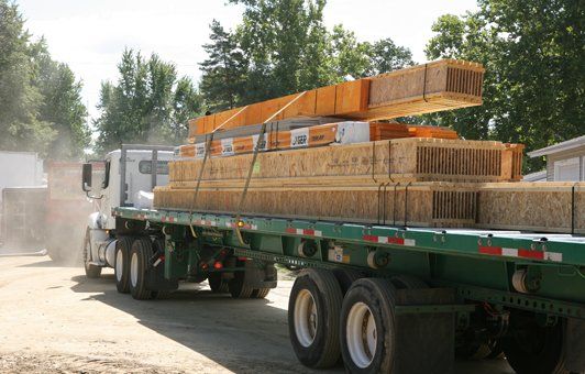 A green semi truck is carrying a load of wooden beams